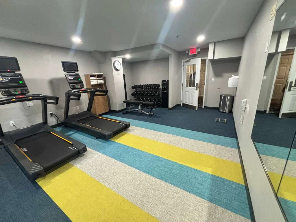 Mirror-lined hotel gym in Weston with treadmills, dumbbell rack, bench, sanitizer and exit door