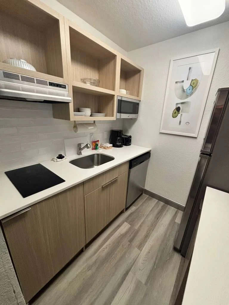 Extended-stay kitchenette with dish storage, two-burner cooktop and stainless appliances in a hotel suite