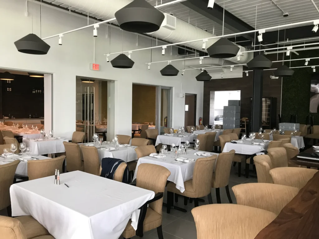 Elegant restaurant dining room with table setup, lighting design and upholstered seating renovated in Miami hospitality project