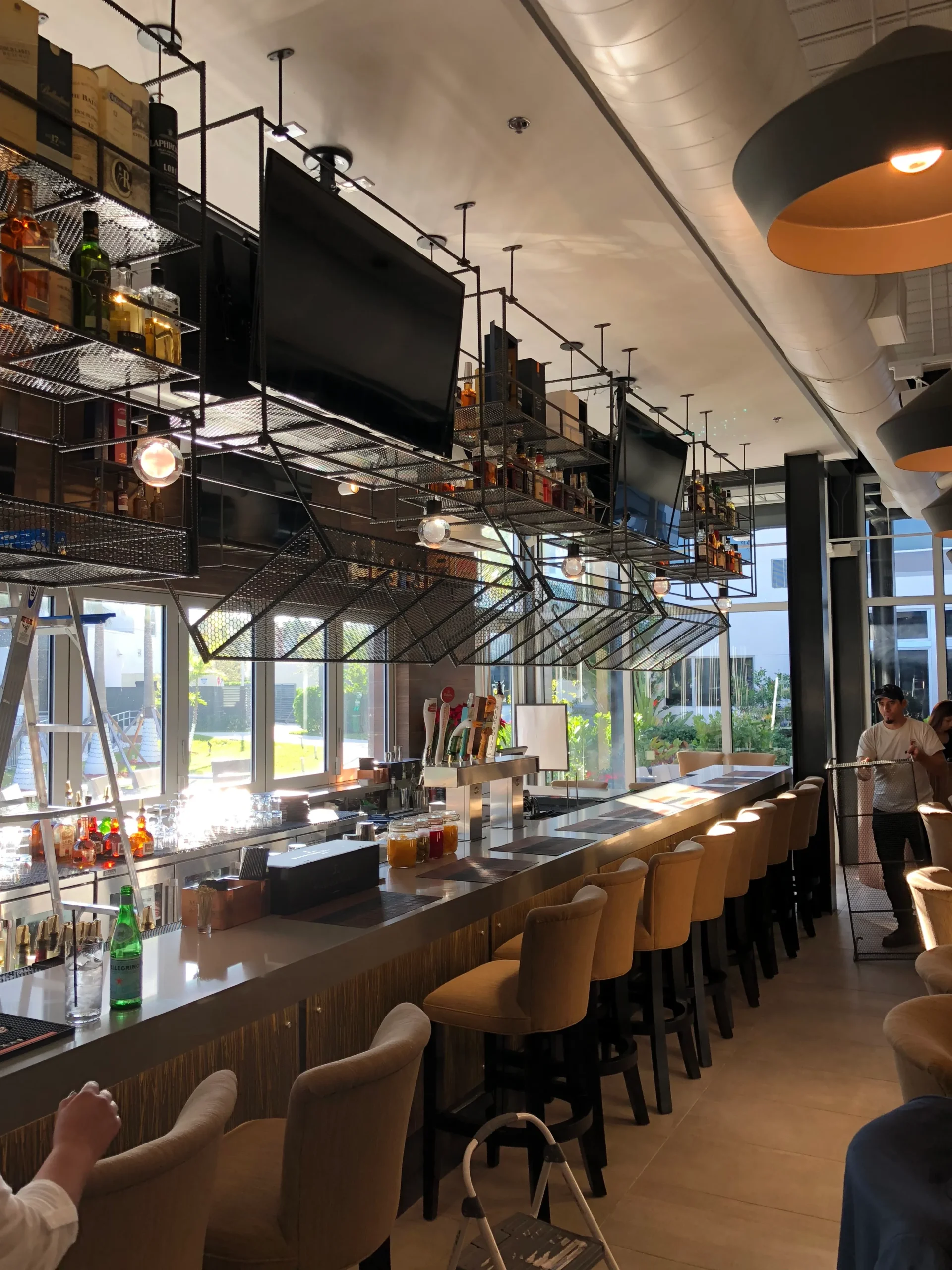Modern restaurant bar with industrial ceiling, suspended shelving and seating built during commercial construction project in Miami